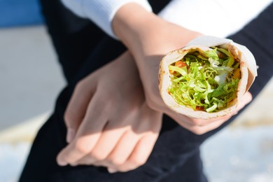 Photo of Woman holding delicious vegetable roll outdoors, closeup