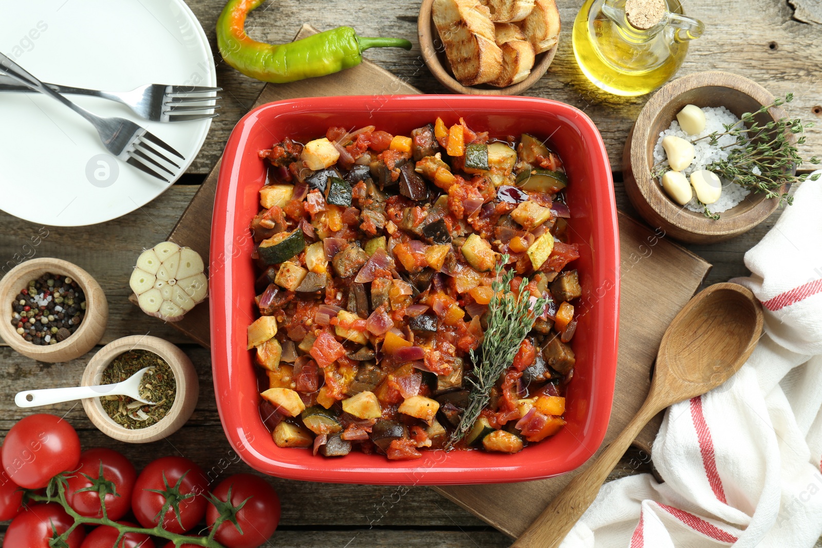 Photo of Dish with tasty ratatouille, ingredients and bread on wooden table, flat lay