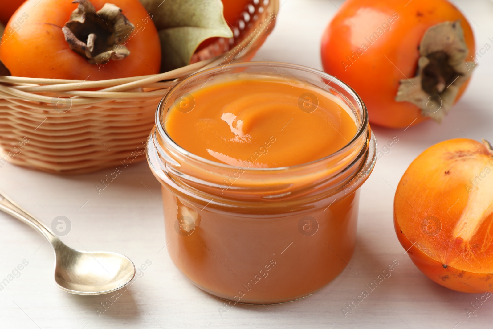 Photo of Delicious persimmon jam in glass jar served on white wooden table, closeup