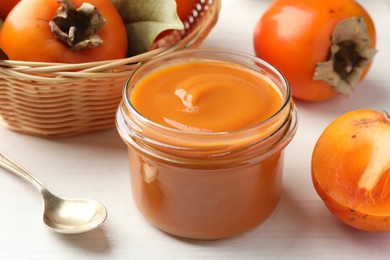 Delicious persimmon jam in glass jar served on white wooden table, closeup