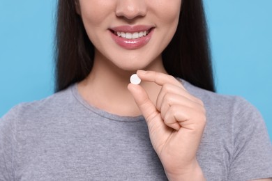 Photo of Woman taking pill on light blue background, closeup