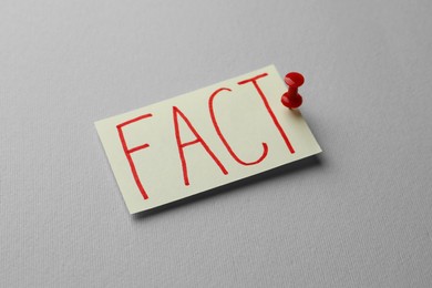 Photo of Sheet of paper with word Fact pinned to grey background, closeup