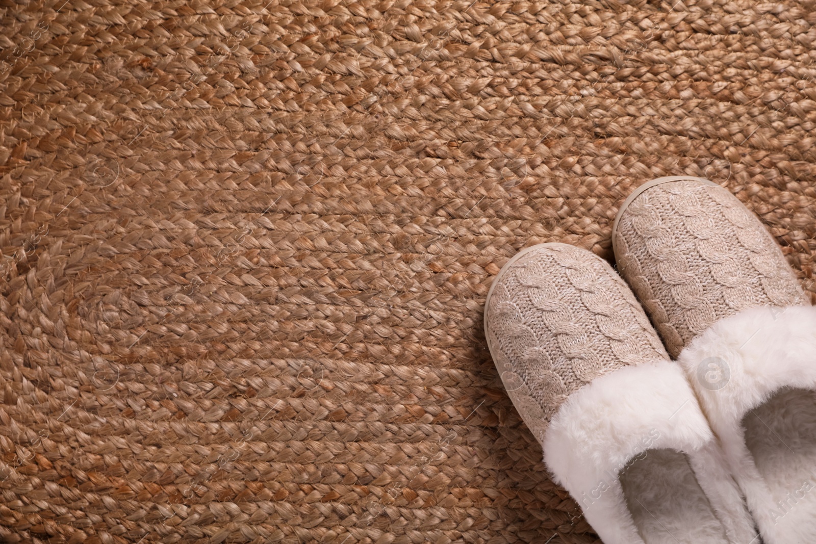 Photo of Pair of warm stylish slippers on wicker carpet, top view. Space for text