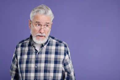 Portrait of surprised senior man on violet background, space for text