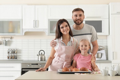 Happy family with tray of freshly oven baked buns at table in kitchen. Space for text