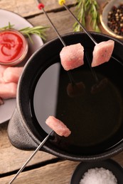 Fondue pot with oil, forks, raw meat pieces and other products on wooden table, flat lay