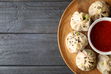 Photo of Wooden plate with tasty baozi dumplings and sauce on wooden background, top view. Space for text