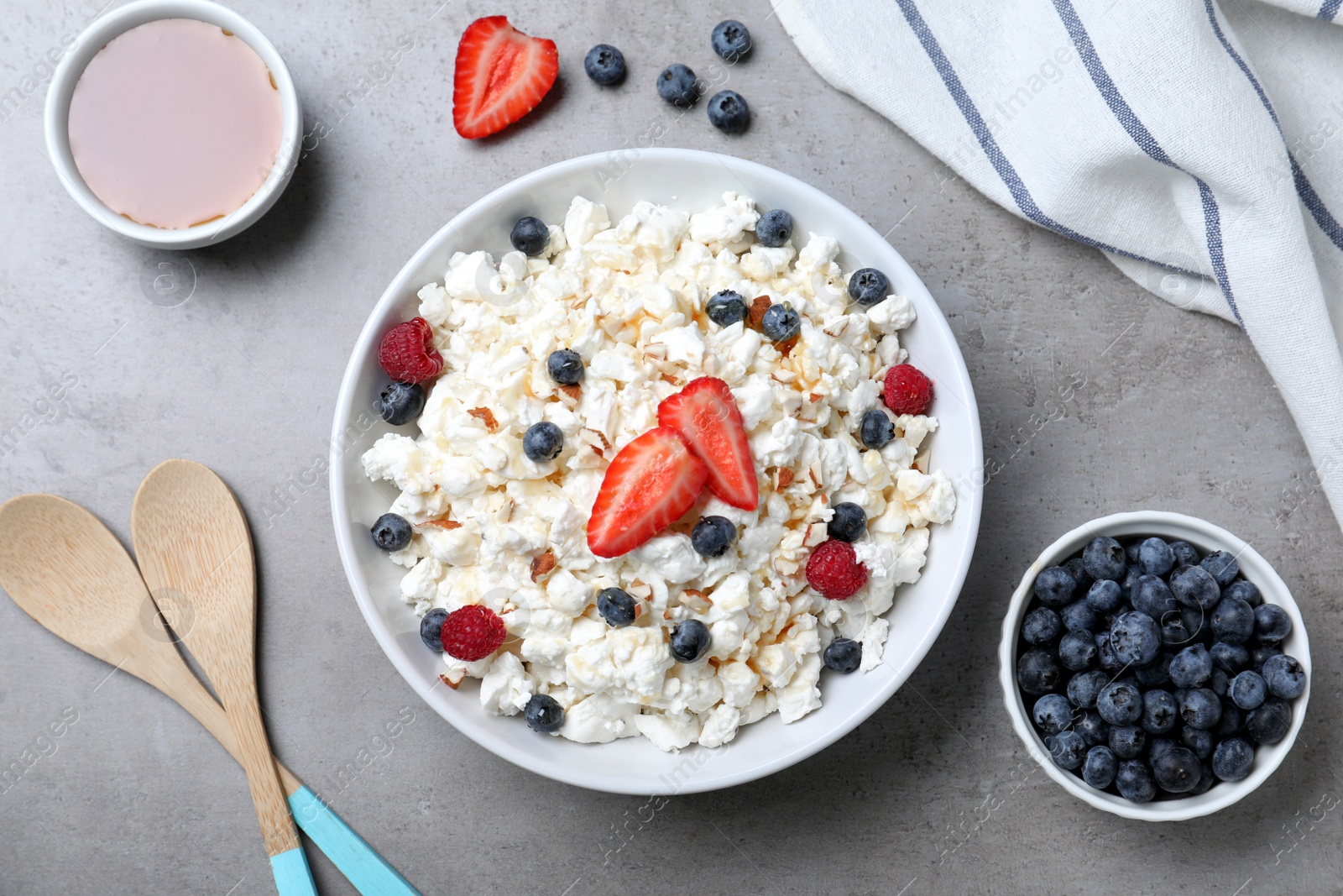 Photo of Delicious cottage cheese with fresh berries and honey served for breakfast on light grey table, flat lay