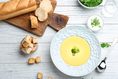 Photo of Bowl of cheese cream soup with broccoli served on white wooden table, flat lay