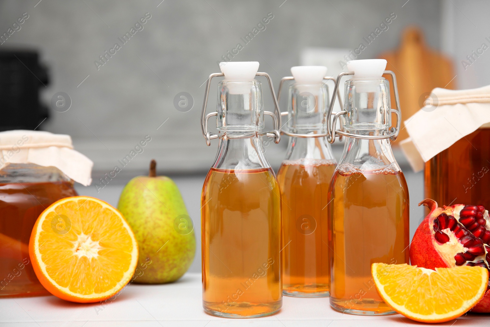 Photo of Homemade fermented kombucha in glass bottles and fresh fruits on white table in kitchen