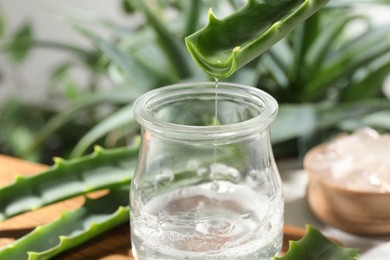 Pouring aloe vera gel from leaf into jar at table, closeup