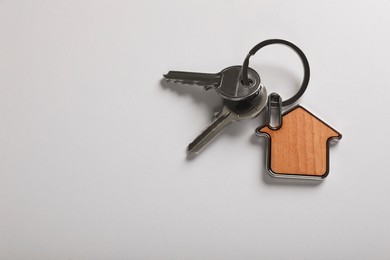 Photo of Keys with trinket in shape of house on white background, top view and space for text. Real estate agent services
