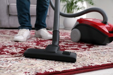 Photo of Man cleaning carpet with vacuum cleaner at home, closeup