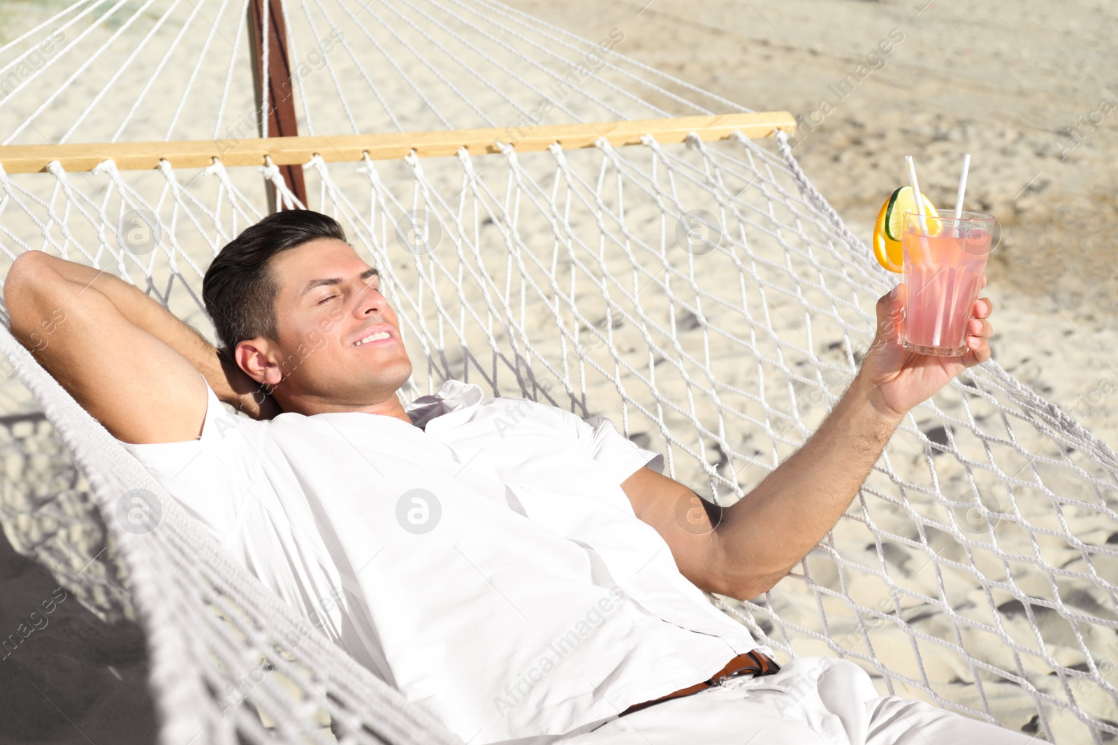 Photo of Man with refreshing cocktail relaxing in hammock on beach