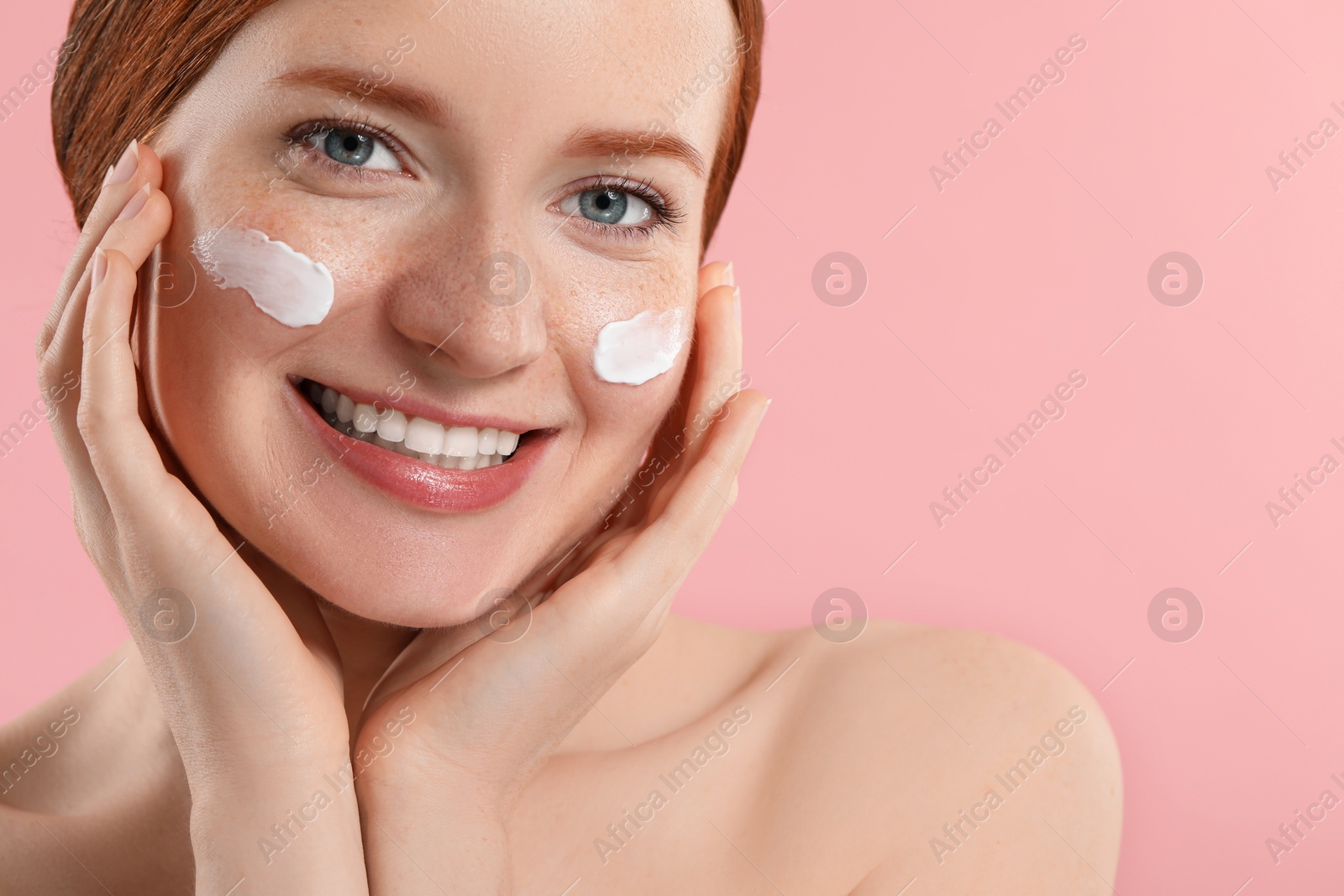 Photo of Smiling woman with freckles and cream on her face against pink background, closeup. Space for text