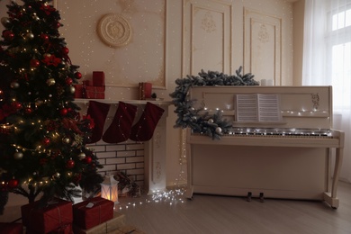 Photo of White piano with music sheets and beautiful Christmas tree in festive room interior