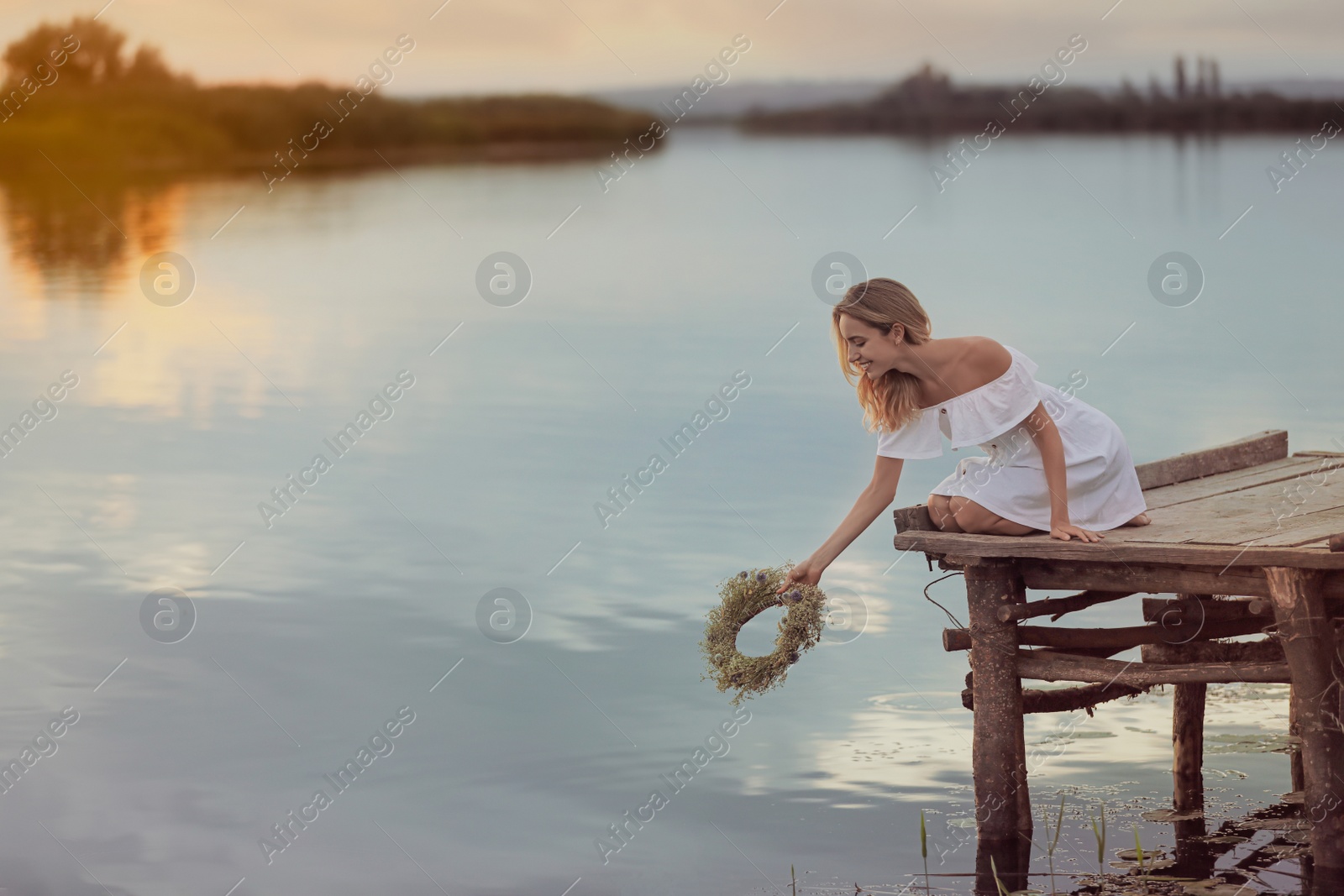 Photo of Young woman putting wreath made of beautiful flowers in water