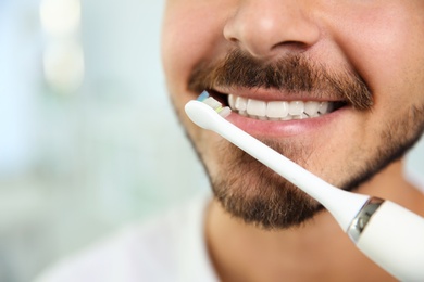 Young man with electric toothbrush on blurred background, closeup. Space for text