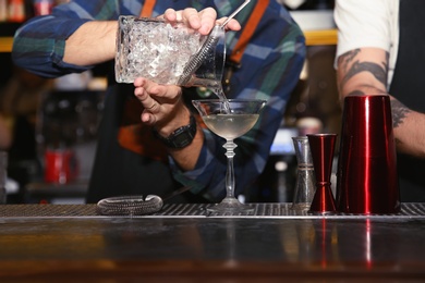 Photo of Bartender pouring tasty cocktail at counter in nightclub, closeup