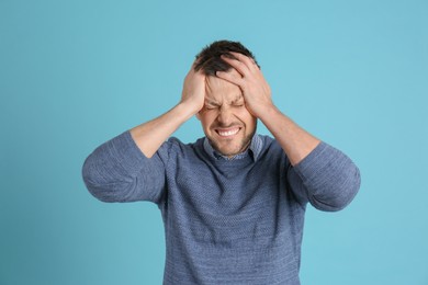 Photo of Man suffering from terrible migraine on light blue background