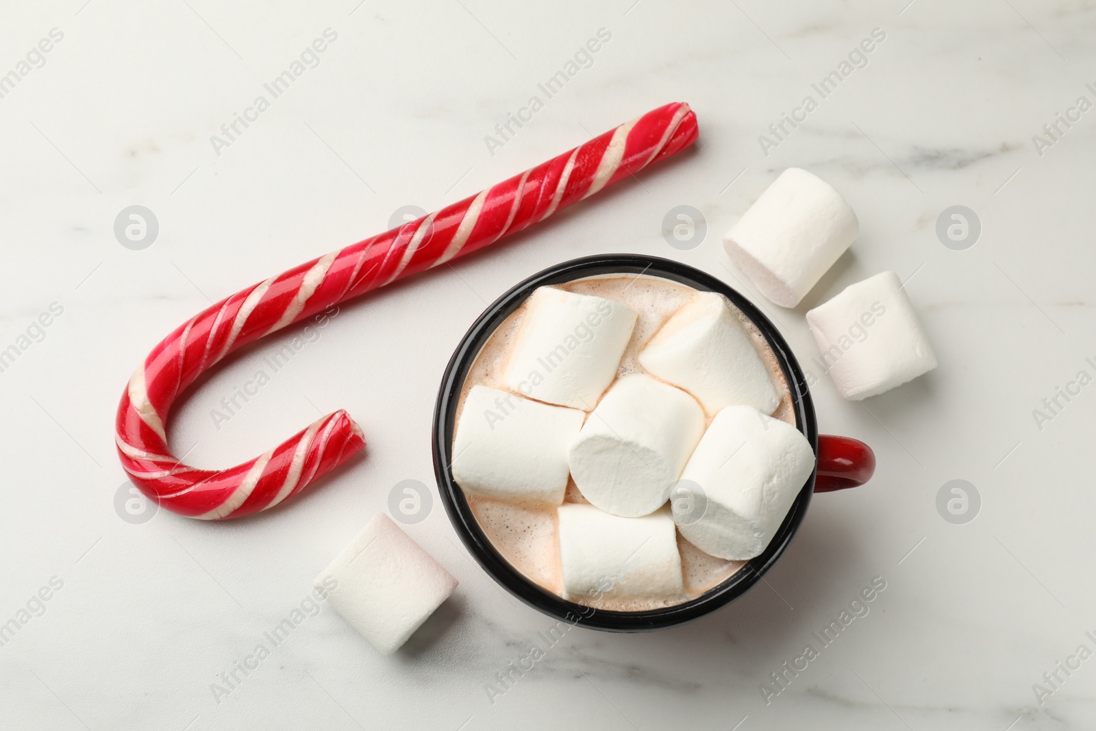 Photo of Tasty hot chocolate with marshmallows and candy cane on white marble table, top view