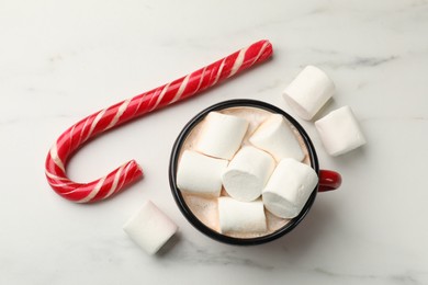 Photo of Tasty hot chocolate with marshmallows and candy cane on white marble table, top view