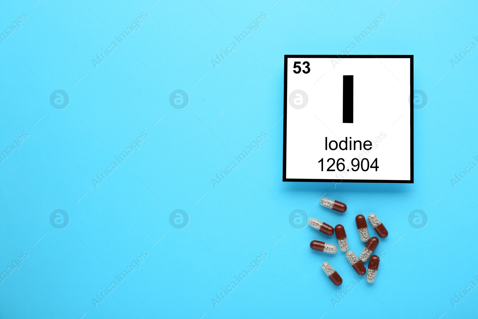 Photo of Card with iodine element and pills on light blue background, flat lay. Space for text
