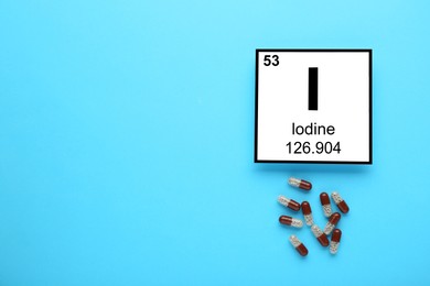 Photo of Card with iodine element and pills on light blue background, flat lay. Space for text