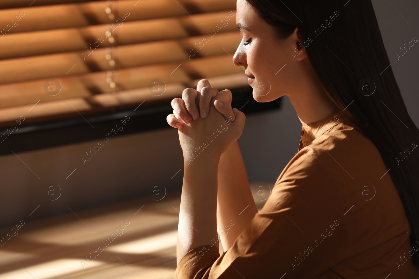 Photo of Religious young woman with clasped hands praying indoors