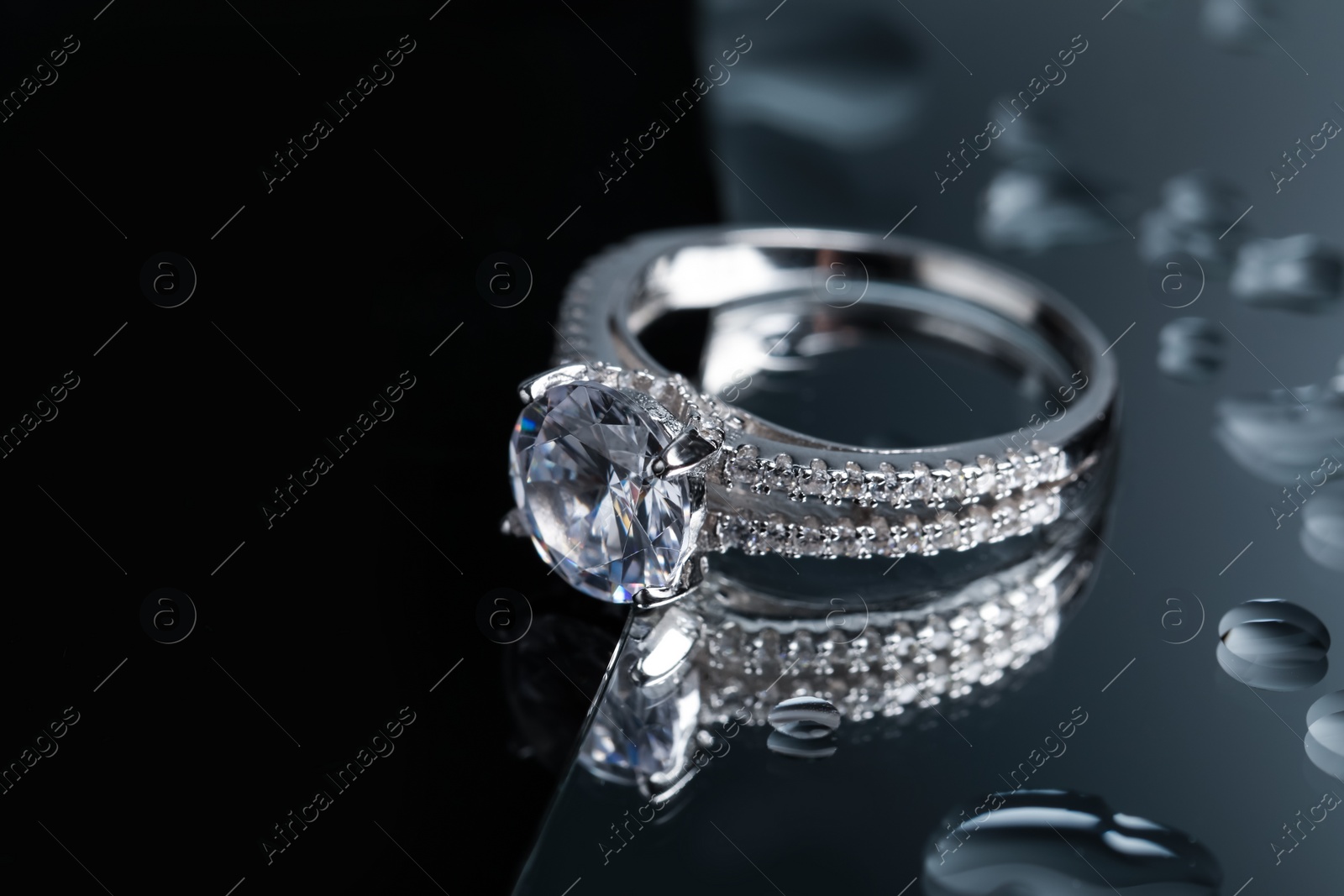 Photo of Luxury jewelry. Stylish presentation of elegant ring on mirror with water drops, closeup. Space for text