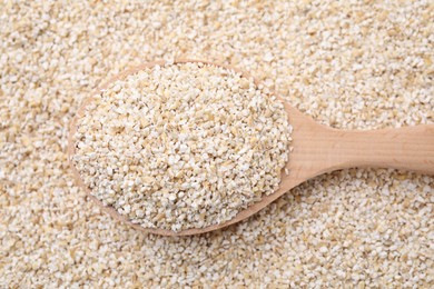 Photo of Wooden spoon on raw barley groats, top view