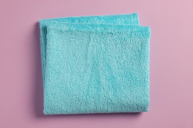 Photo of Soft folded light blue towel on violet background, top view