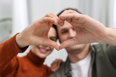 Photo of Happy couple making heart with hands indoors, selective focus