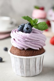 Photo of Delicious cupcake with cream and blueberries on light grey table, closeup