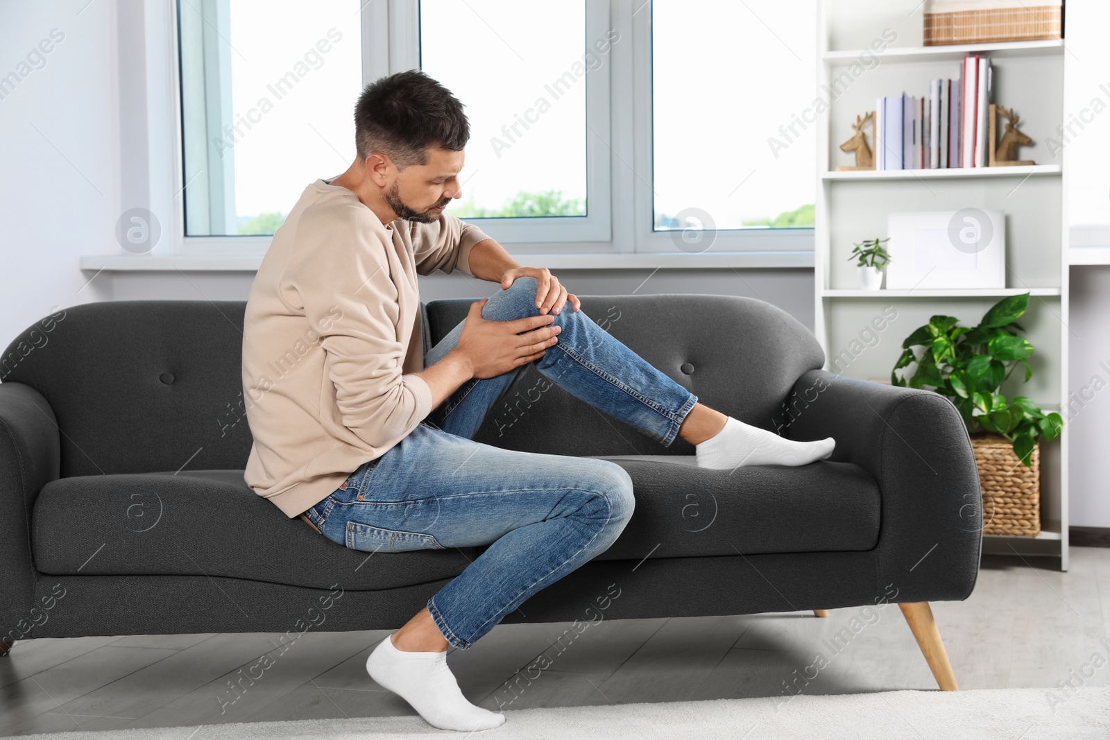 Photo of Man suffering from knee pain on sofa at home
