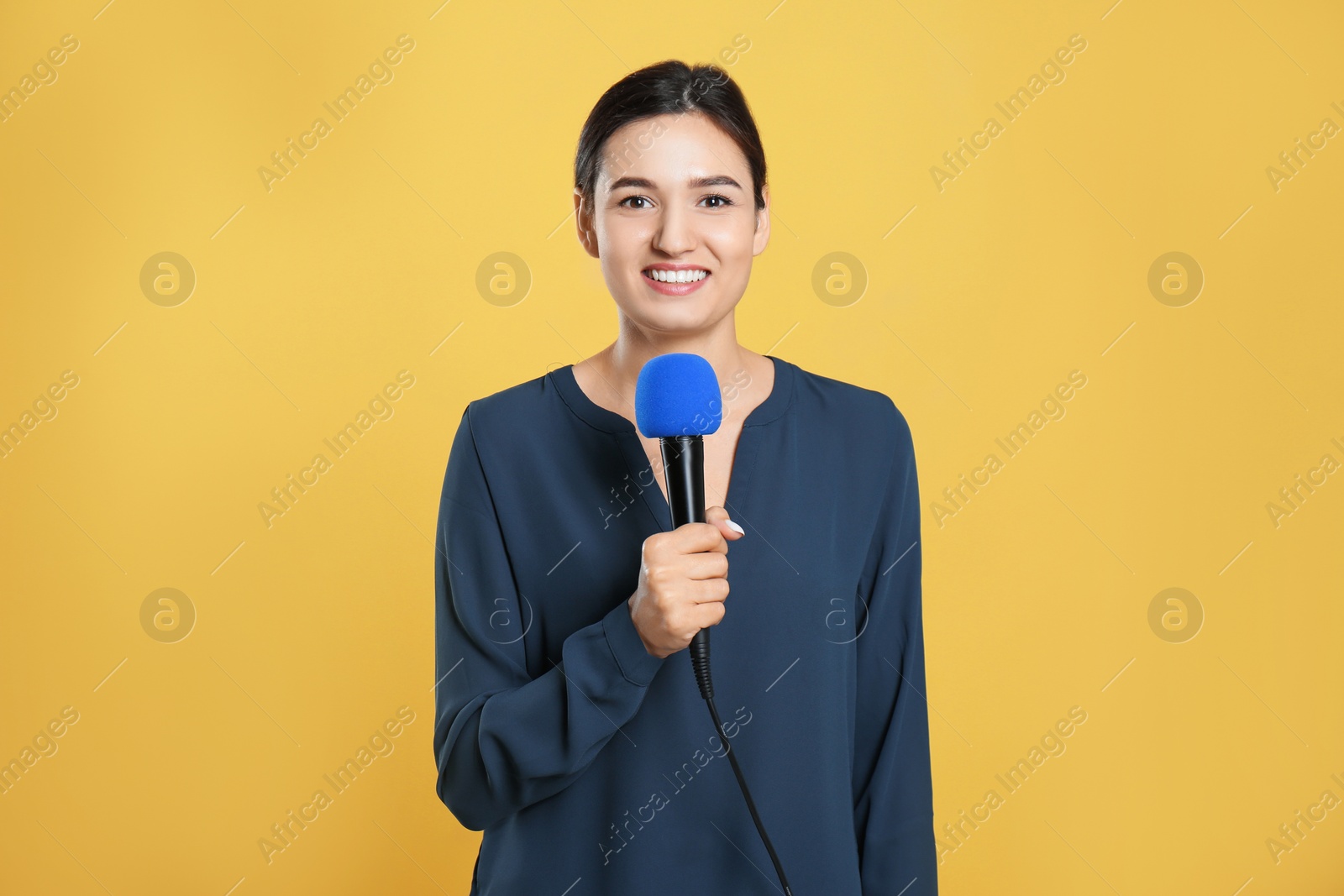 Photo of Young female journalist with microphone on yellow background