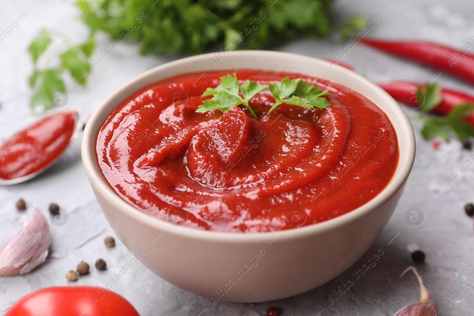 Photo of Organic ketchup and parsley in bowl on grey table, closeup. Tomato sauce