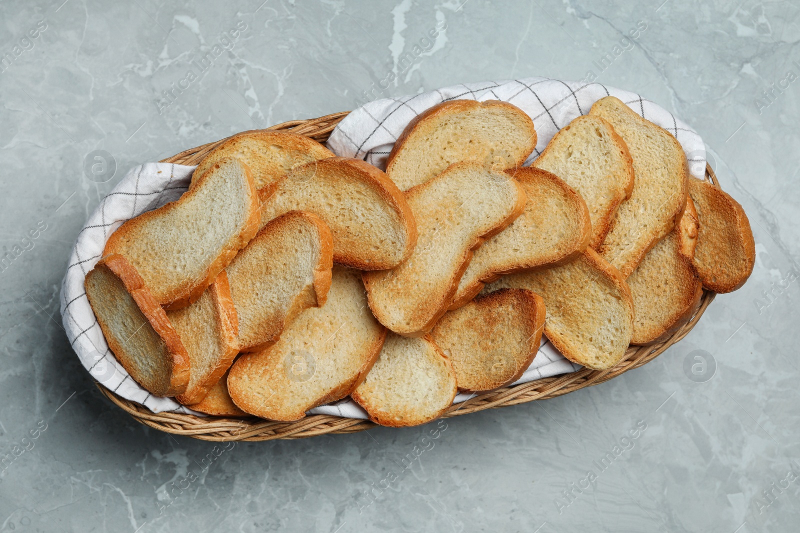 Photo of Basket with toasted bread on grey table, top view