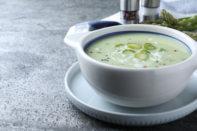 Photo of Bowl of delicious asparagus soup on grey table, space for text