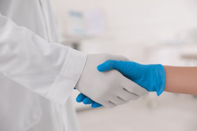 Doctors in medical gloves giving handshake at hospital, closeup