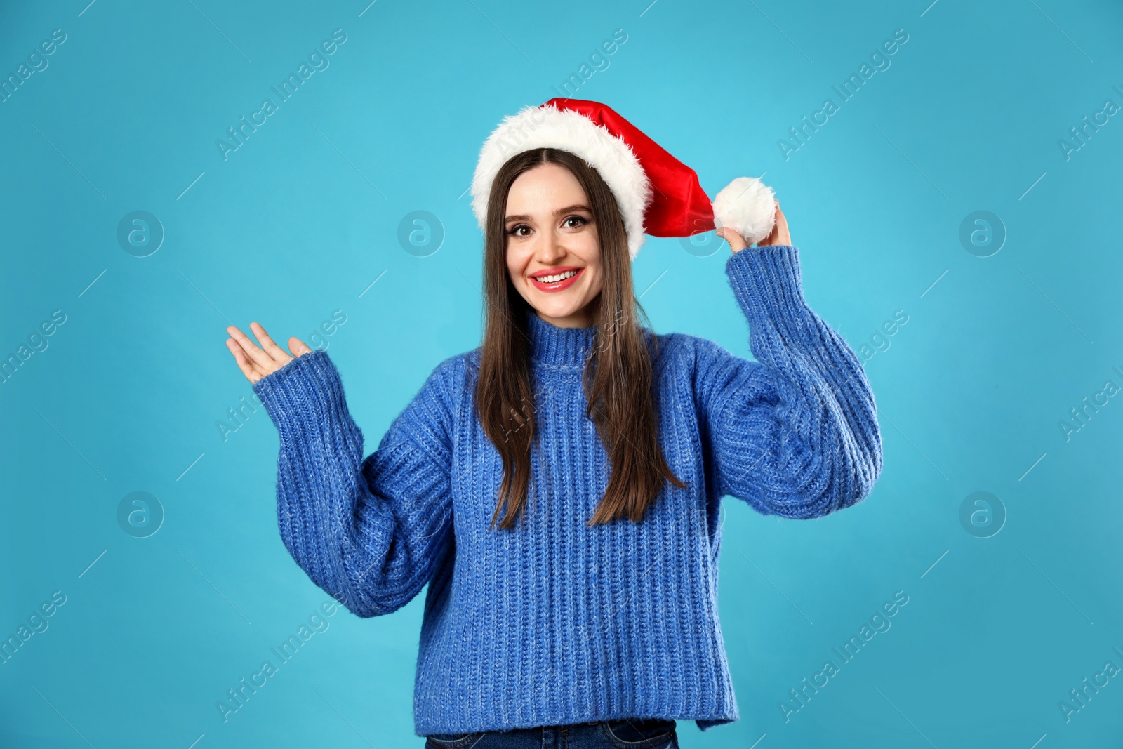 Photo of Young woman wearing Christmas sweater and Santa hat on blue background