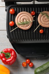 Photo of Electric grill with homemade sausages, rosemary and vegetables on rustic wooden table, flat lay