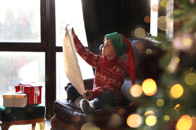 Photo of Little boy with wish list to Santa Claus near window indoors. Christmas holiday