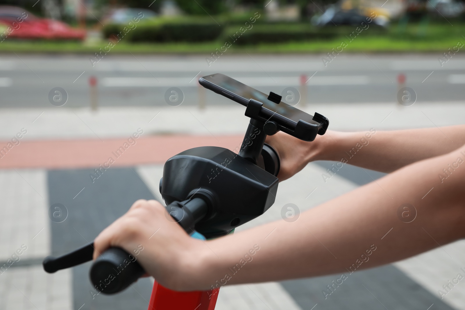 Photo of Woman riding modern electric kick scooter with smartphone outdoors