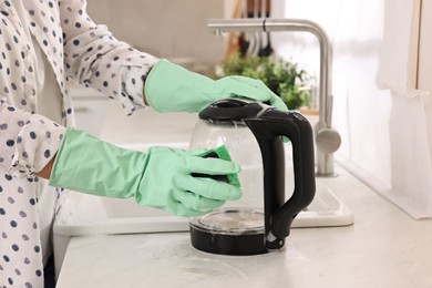 Woman cleaning electric kettle with sponge at countertop in kitchen, closeup