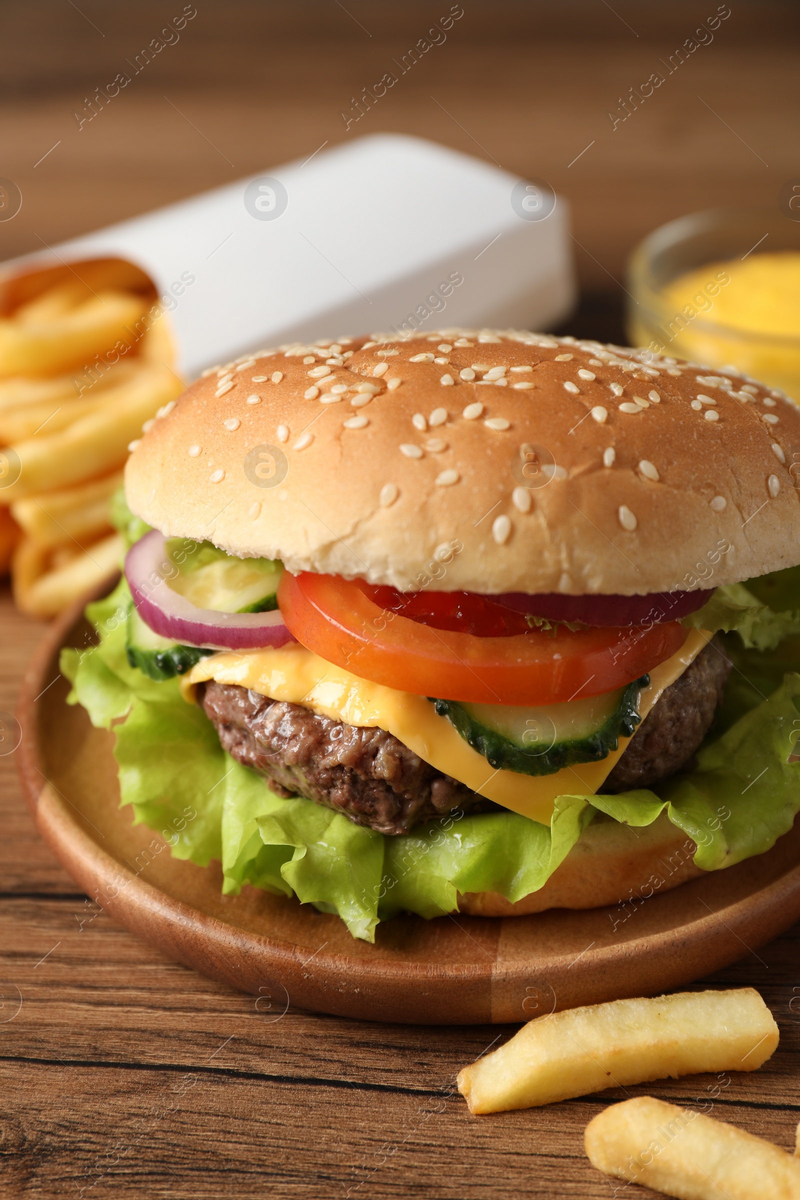 Photo of Delicious burger, sauce and french fries served on wooden table, closeup