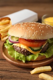 Photo of Delicious burger, sauce and french fries served on wooden table, closeup