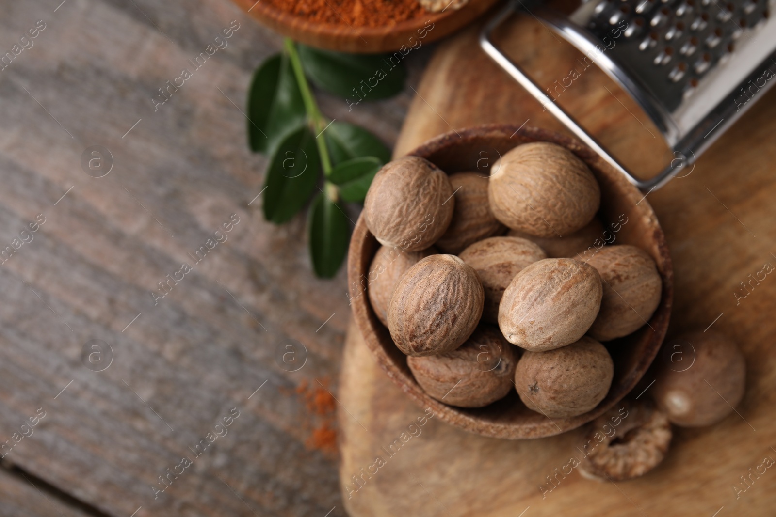 Photo of Nutmegs in bowl and grater on wooden table, flat lay. Space for text