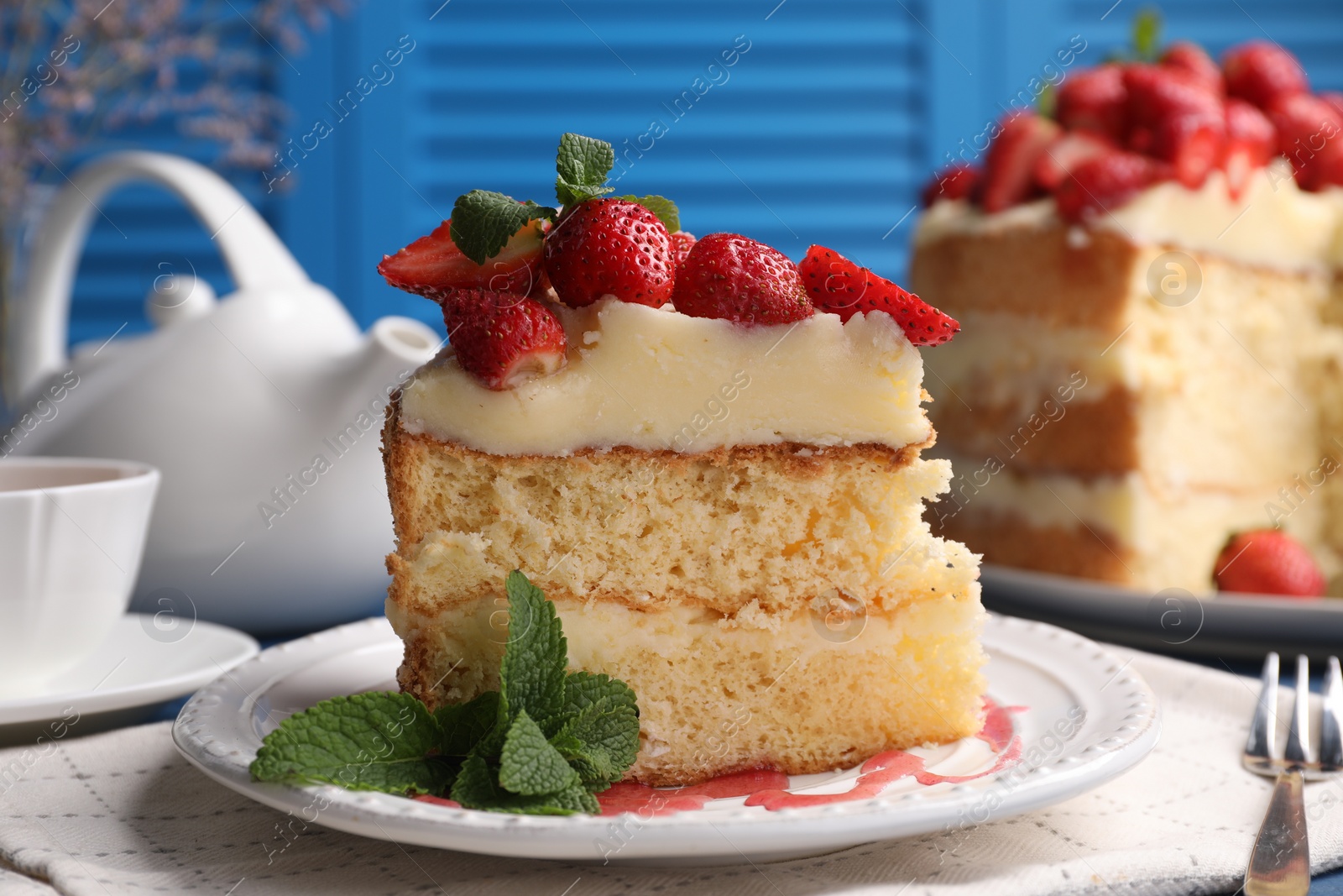 Photo of Piece of tasty cake with fresh strawberries, mint and cup of tea on table, closeup
