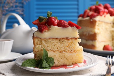 Photo of Piece of tasty cake with fresh strawberries, mint and cup of tea on table, closeup